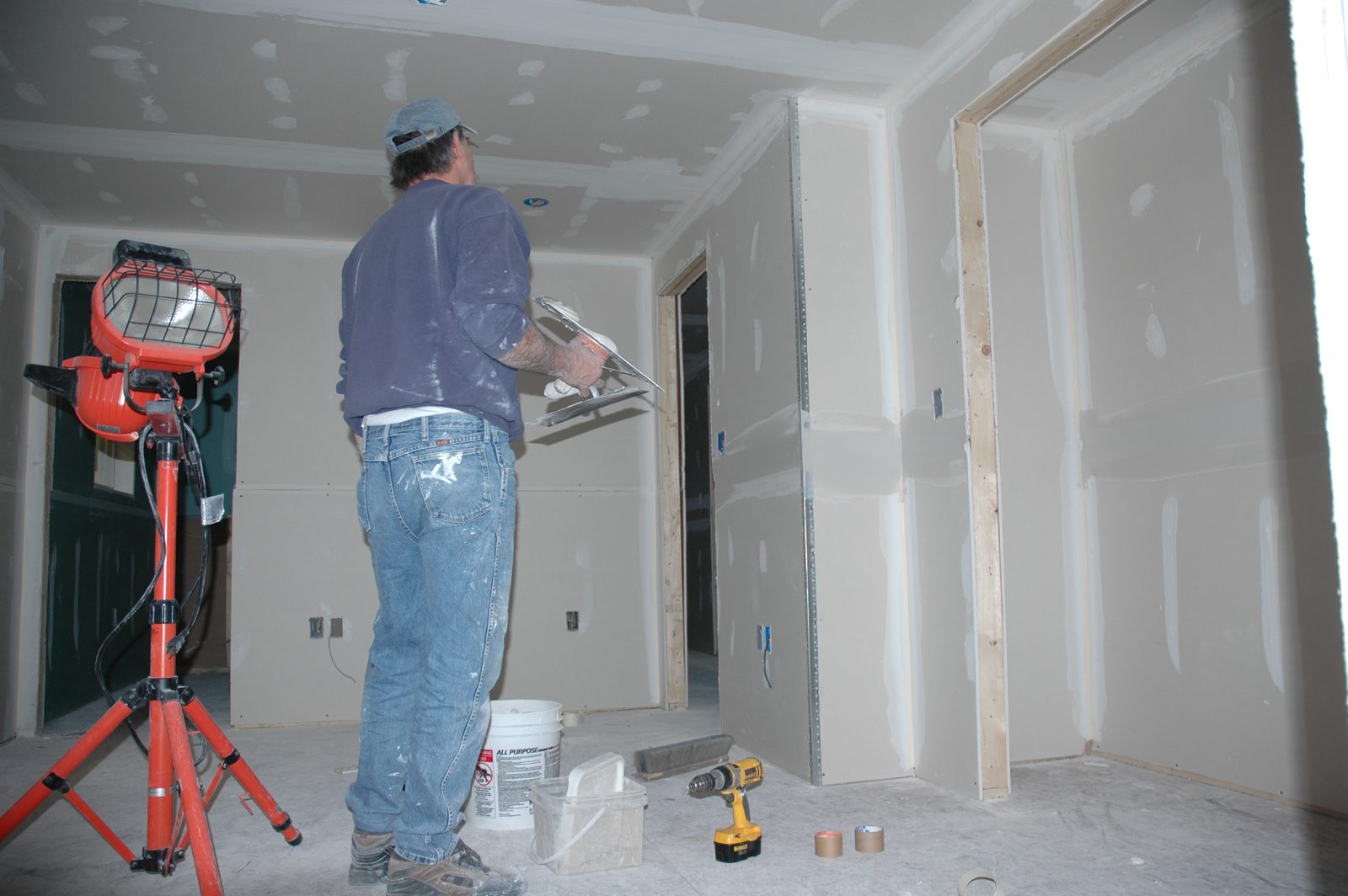 Carpenter finishing new drywall joints in a rebuilt room under a work light