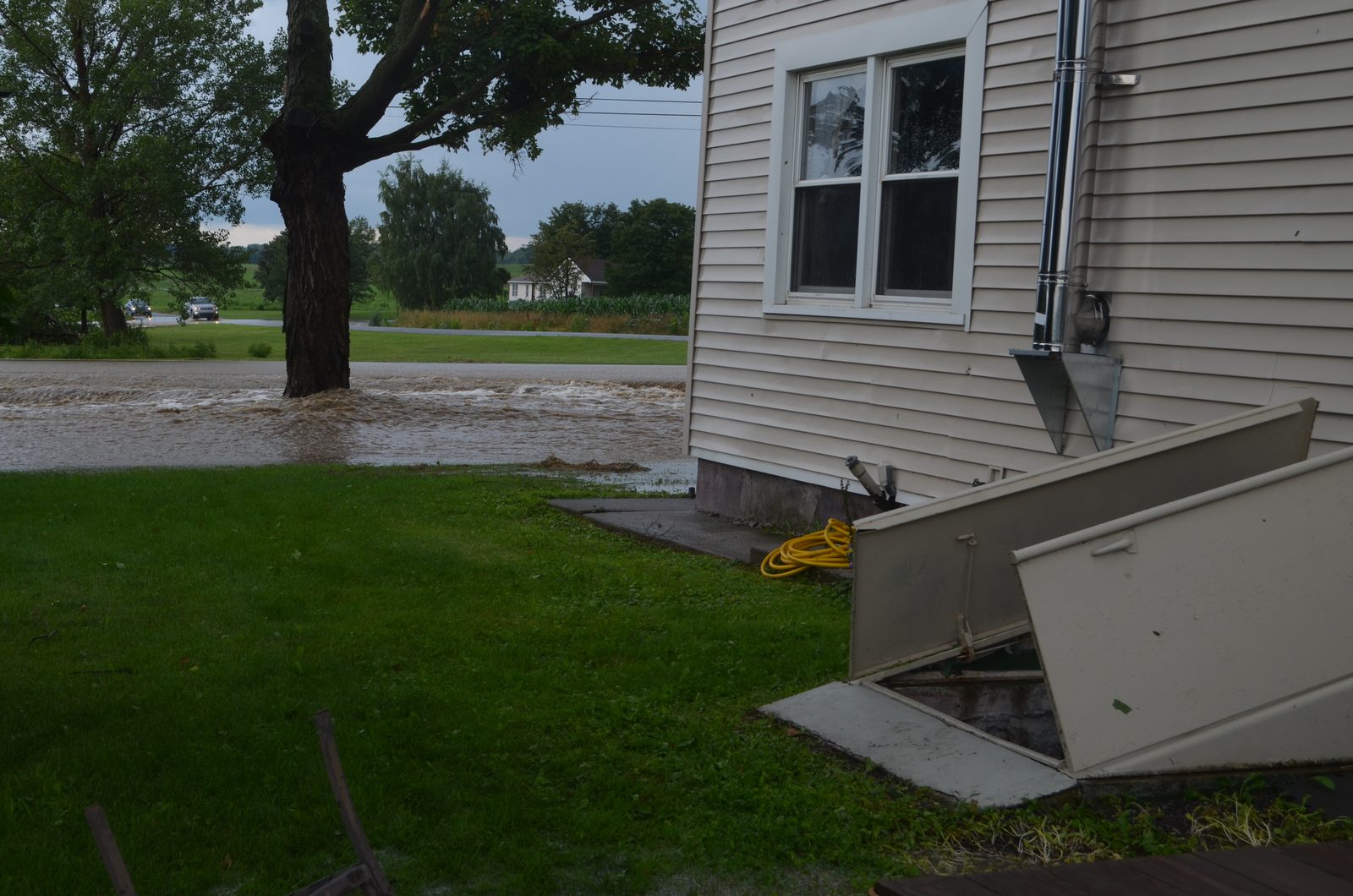 Flooded street beside a house with the basement cellar door open after a storm